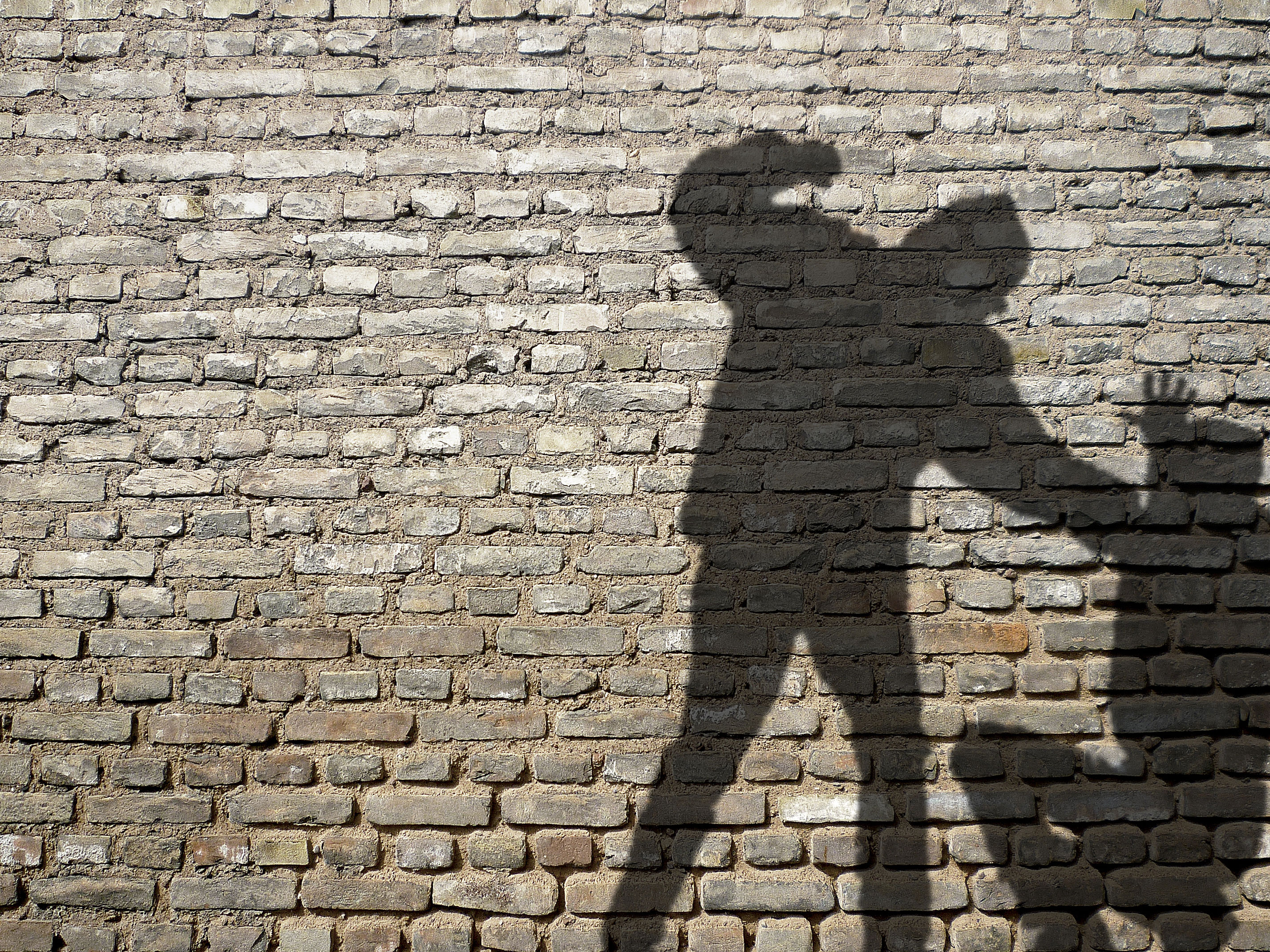 Mauer mit Schatten von zwei Personen, eine Person hebt Faust in Richtung sitzender Person